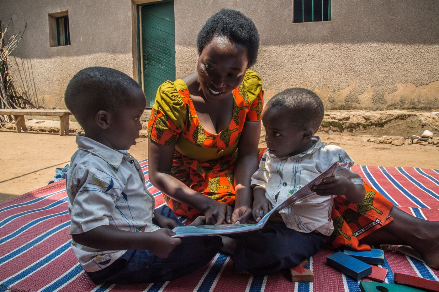 A caregiver reading with two young boys in Kenya